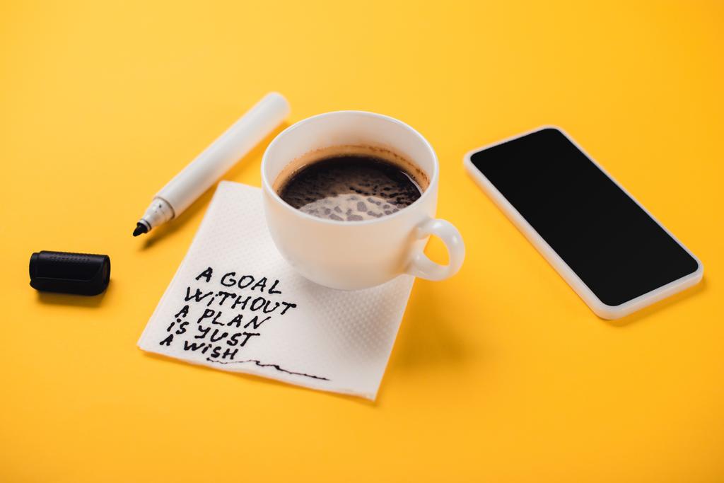 Kâğıt peçeteli kahve fincanı ve plansız bir şekilde sadece yazı, akıllı telefon ve sarı masadaki keçeli kalem. - Fotoğraf, Görsel