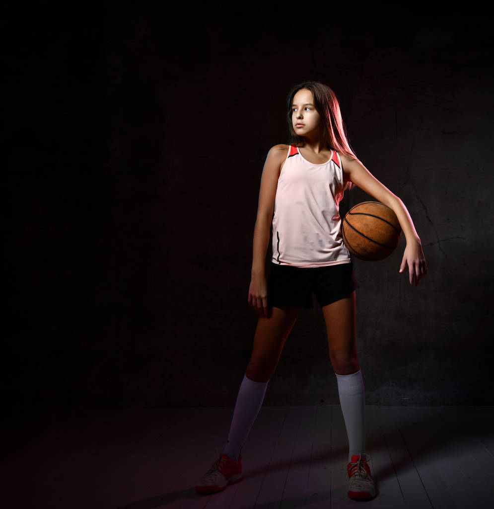 schöne kaukasische Teenagerin in Sportbekleidung beim Basketballspielen. Sportkonzept isoliert auf schwarzem Hintergrund. - Foto, Bild