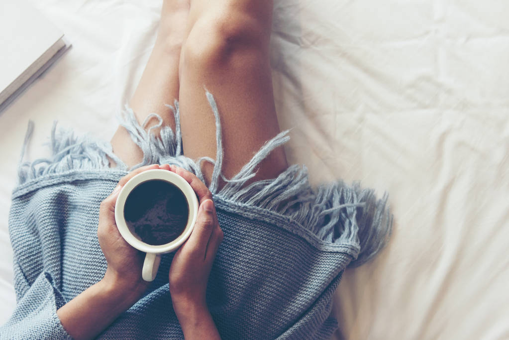 Close-up Beine Frauen auf weißen Bett im Schlafzimmer. Frauen, die morgens Bücher lesen und Kaffee trinken, entspannen sich in der Winterzeit. Lifestyle-Konzept. - Foto, Bild