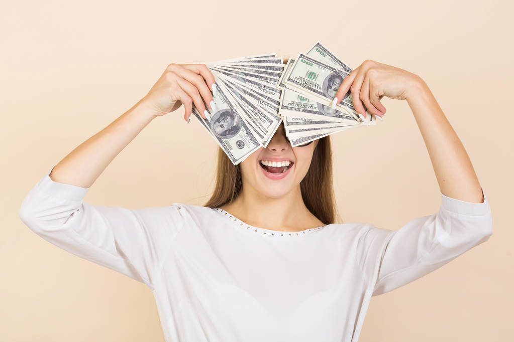 mooie jonge vrouw in bril op een beige achtergrond met dollars in handen - Foto, afbeelding