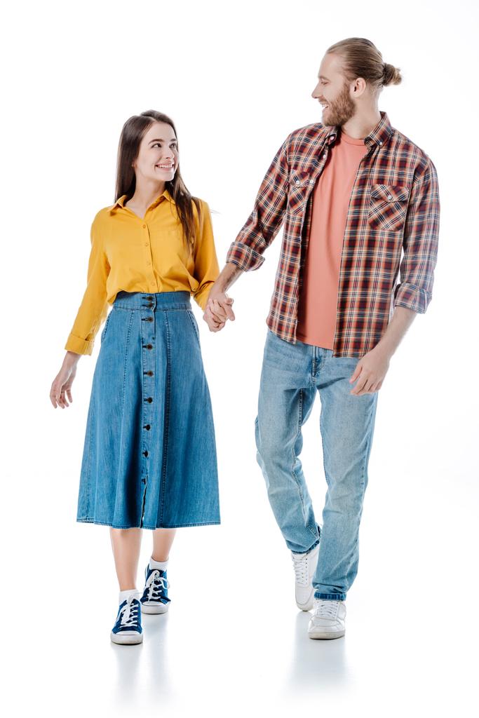 plná délka pohled na šťastný mladý pár v ležérní oblečení chůze a držení se za ruce izolované na bílém - Fotografie, Obrázek
