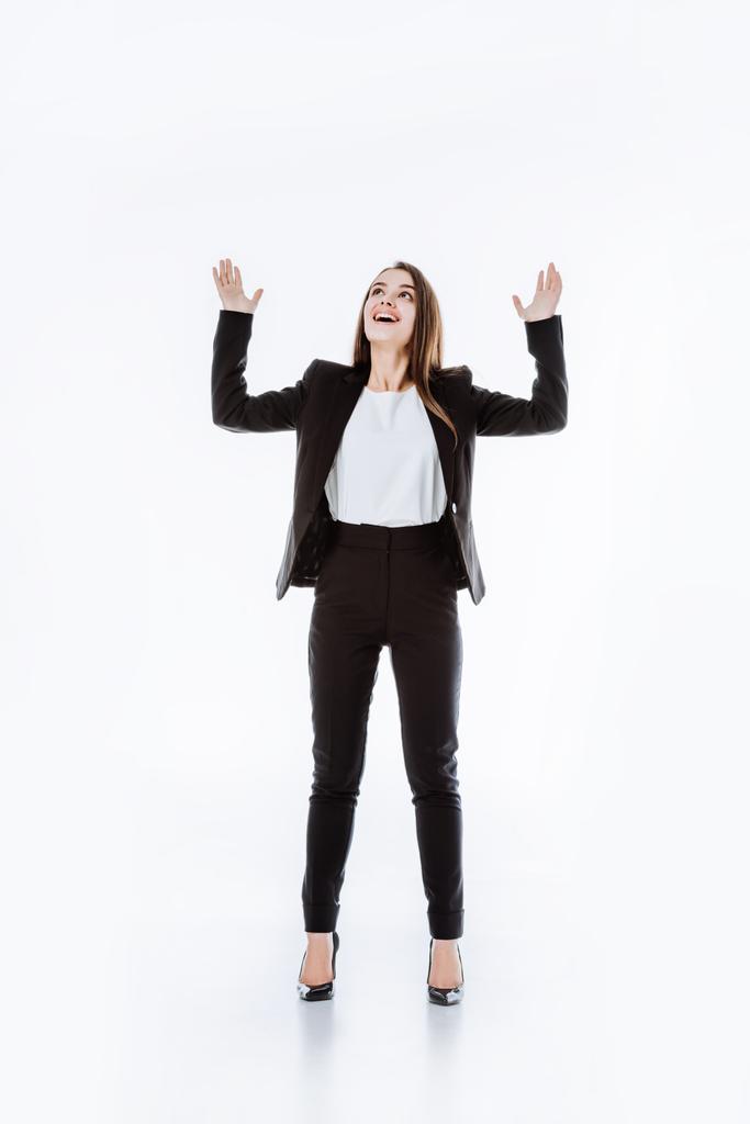 szczęśliwy businesswoman w garniturze z podniesionymi rękami patrząc w górę odizolowany na białym - Zdjęcie, obraz