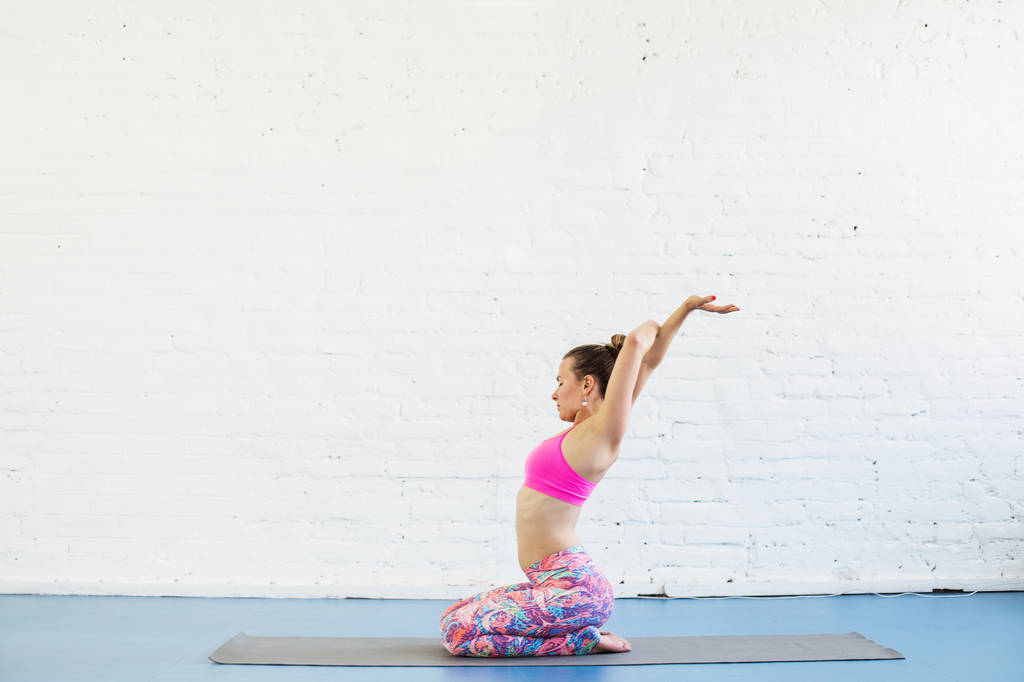 Flexibele vrouw doet yoga-oefeningen in de studio. Witte bakstenen muur op achtergrond  - Foto, afbeelding