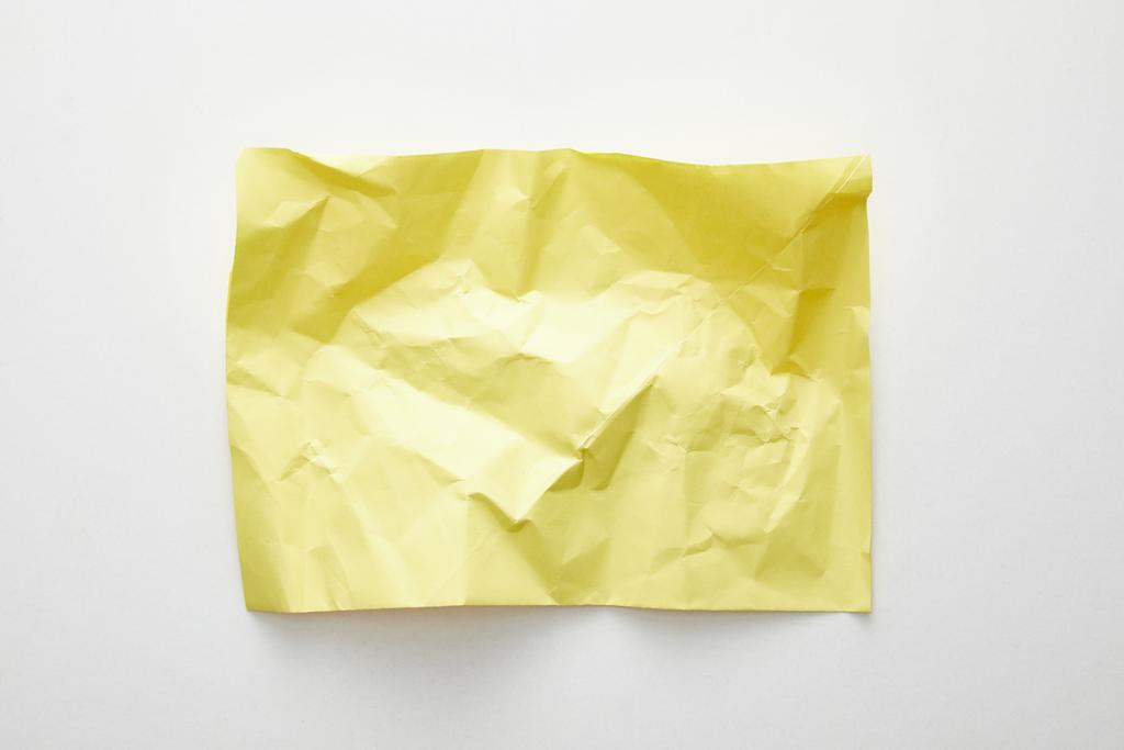 Draufsicht auf leeres zerknülltes gelbes Papier auf weißem Hintergrund - Foto, Bild