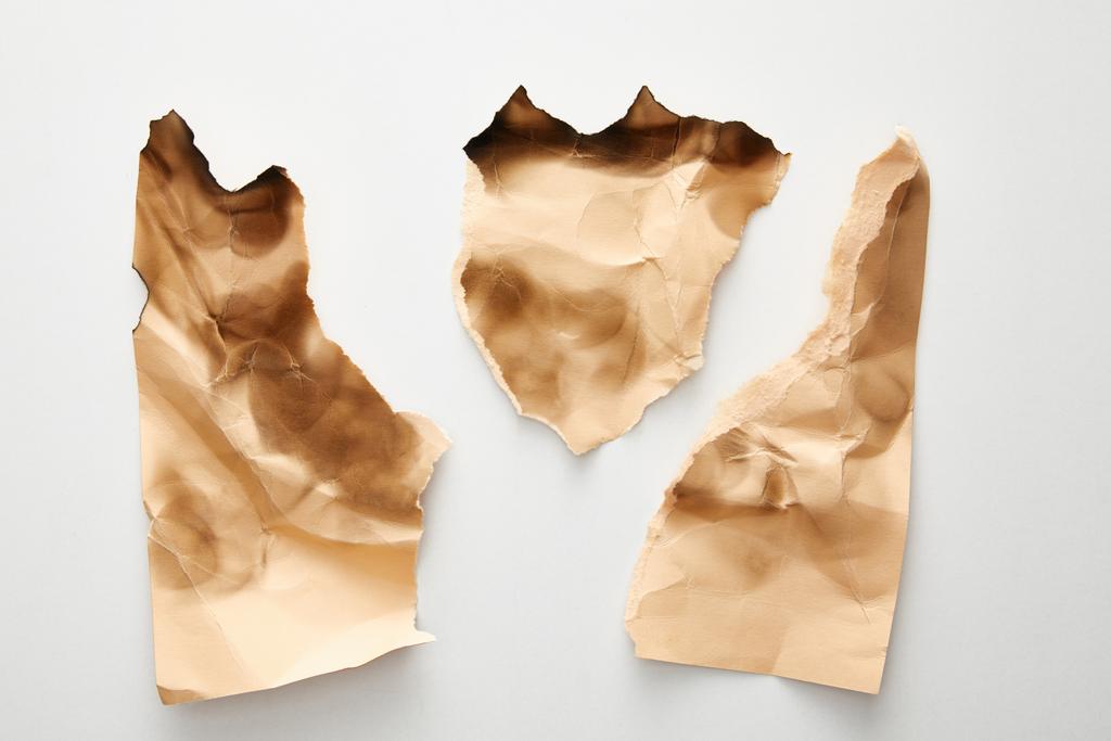 вид сверху на пустой скомканный и обгорелый бежевый лист бумаги на белом фоне
 - Фото, изображение