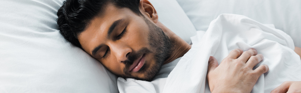 Yakışıklı, çift ırklı adamın sabahları yatakta uyuduğu panoramik bir çekim.  - Fotoğraf, Görsel