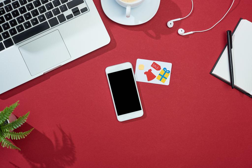 Ansicht der Kreditkarte auf rotem Hintergrund mit Smartphone, Laptop, Kopfhörer und Kaffee - Foto, Bild
