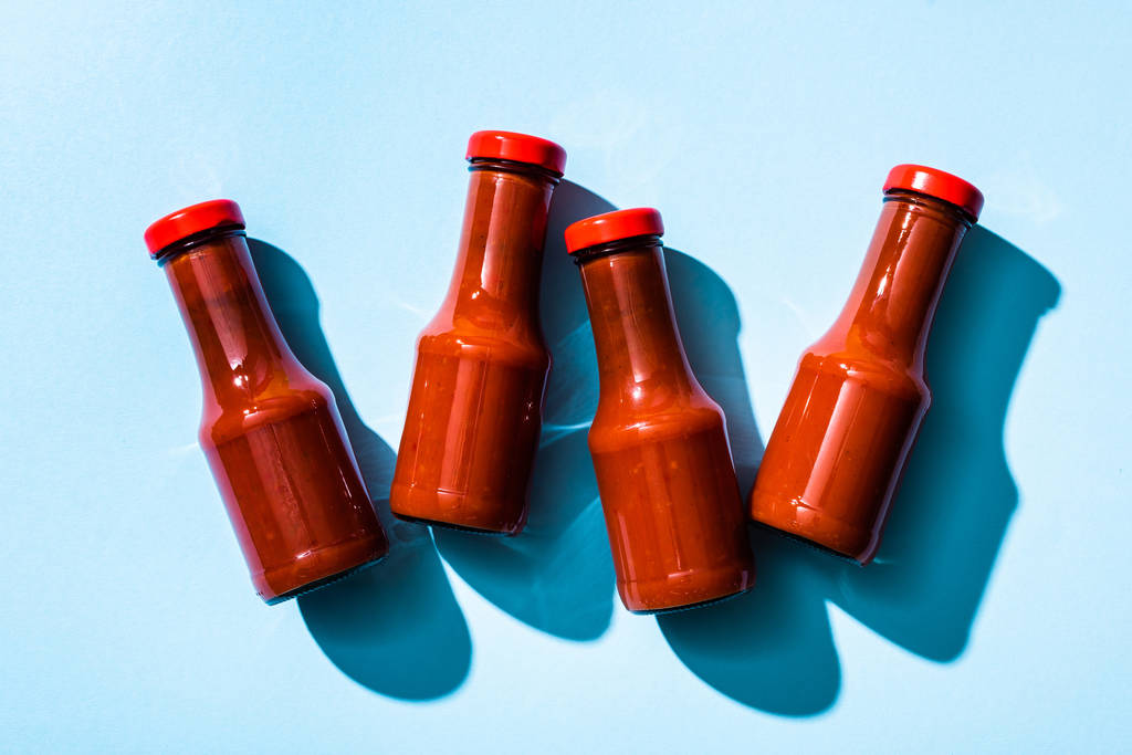 Widok z góry sosu pomidorowego w butelkach z cieniem na niebieskim tle - Zdjęcie, obraz