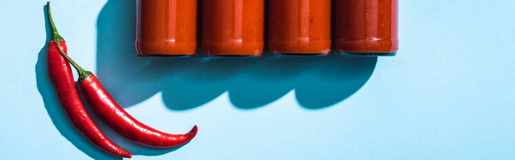 Vista superior de botellas con salsa de chile y chiles sobre fondo azul, plano panorámico
 - Foto, Imagen