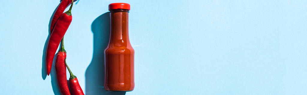Top view of tasty chili sauce with chili peppers on blue background, panoramic shot - Photo, Image