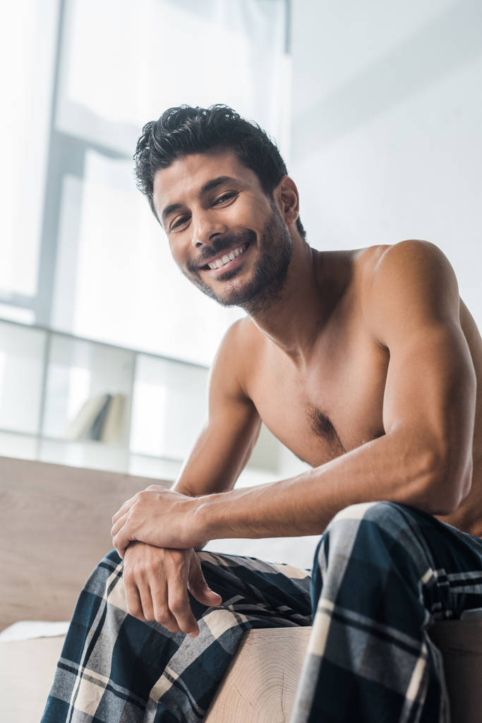 bajo ángulo vista de guapo y sexy bi-racial hombre sonriendo a la cámara en la mañana
  - Foto, imagen