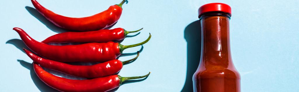 Top kilátás érett chili paprika és chili szósz üveg kék háttér, panoráma lövés - Fotó, kép