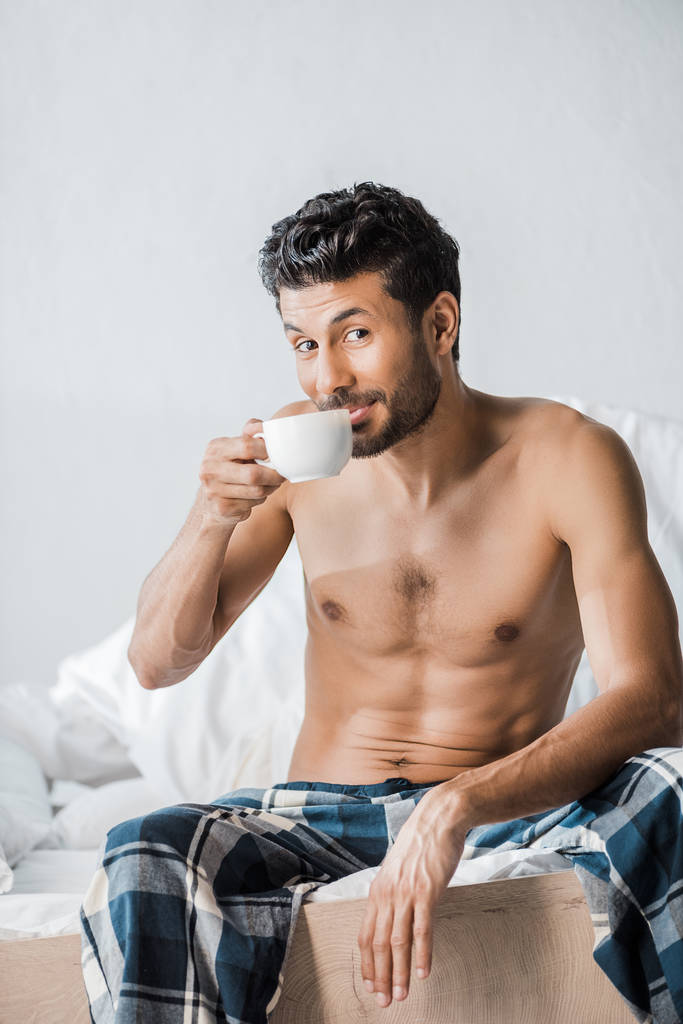 Красивый и улыбающийся бирасовый мужчина пьет кофе по утрам.
  - Фото, изображение