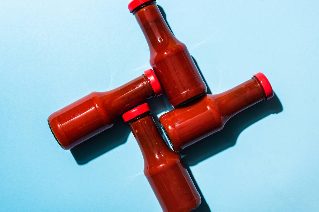 Draufsicht auf köstlichen Ketchup in Flaschen auf blauem Hintergrund - Foto, Bild