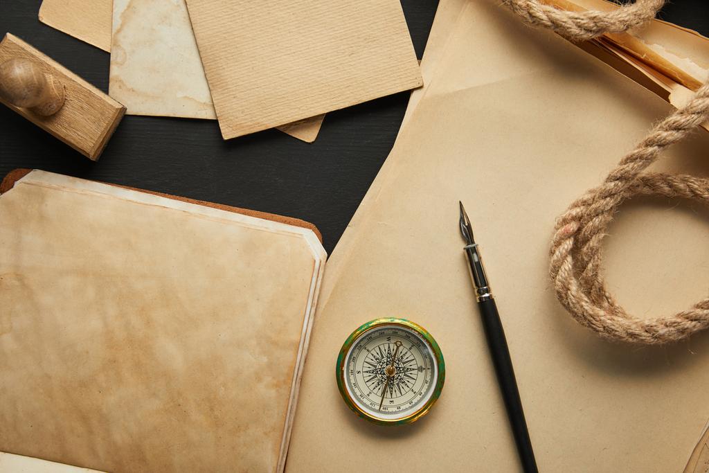ylhäältä näkymä vintage paperi, köysi, kompassi, leima ja mustekynä mustalla taustalla
 - Valokuva, kuva