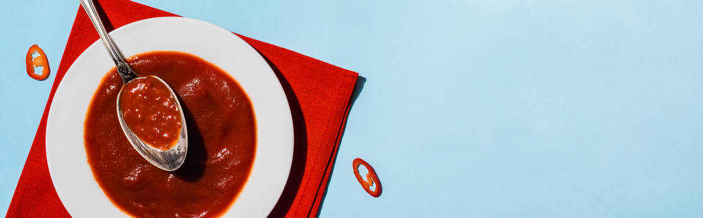 Top pohled na domácí chilli omáčka s plátky chilli pepře na modrém pozadí, panoramatický výstřel - Fotografie, Obrázek