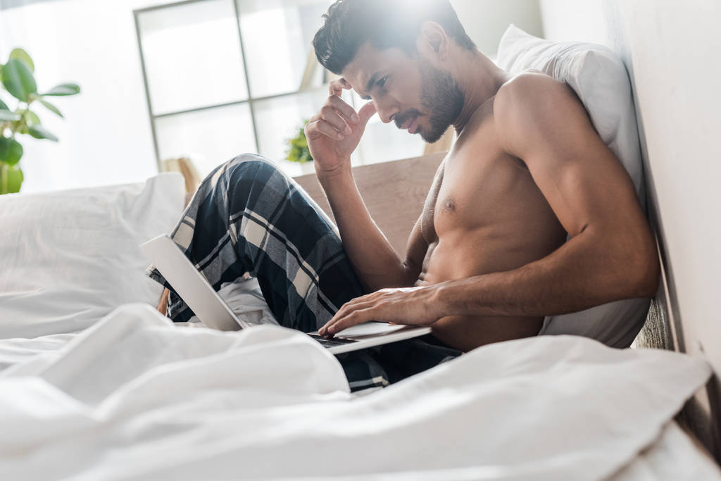 vista lateral del hombre bi-racial guapo y pensativo usando el ordenador portátil en la mañana
  - Foto, imagen