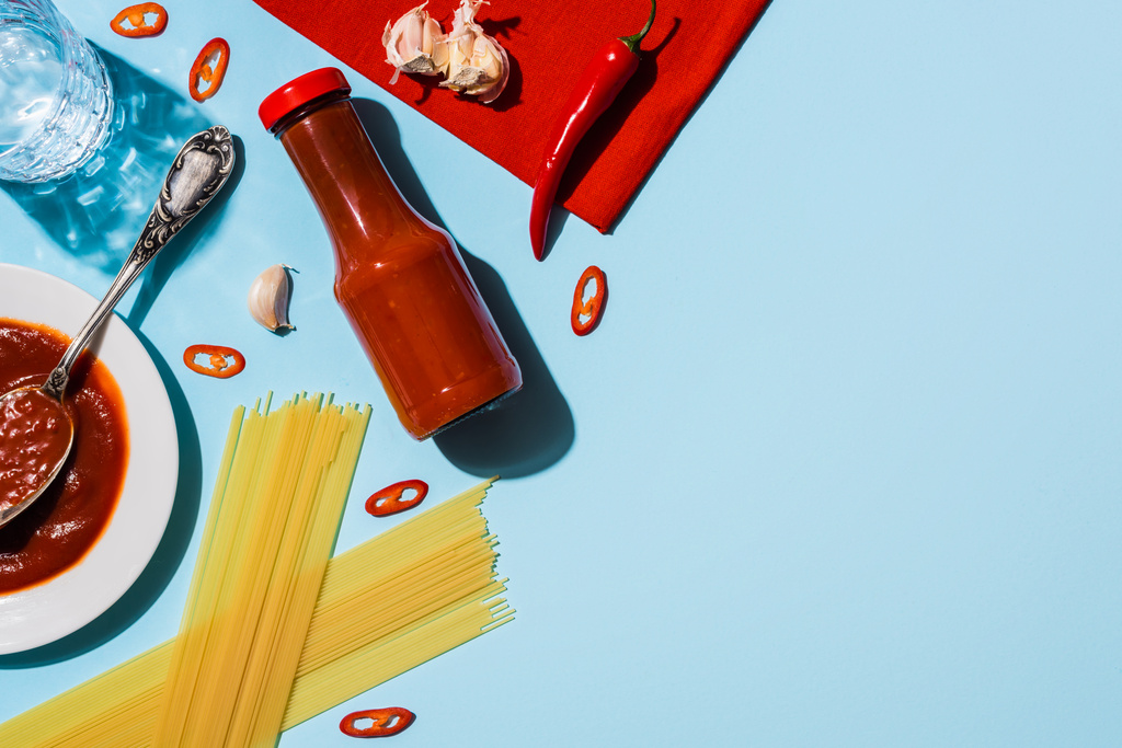 Top näkymä mausteinen ketsuppi valkosipuli ja chili pippuri vieressä spagetti sinisellä pohjalla
 - Valokuva, kuva