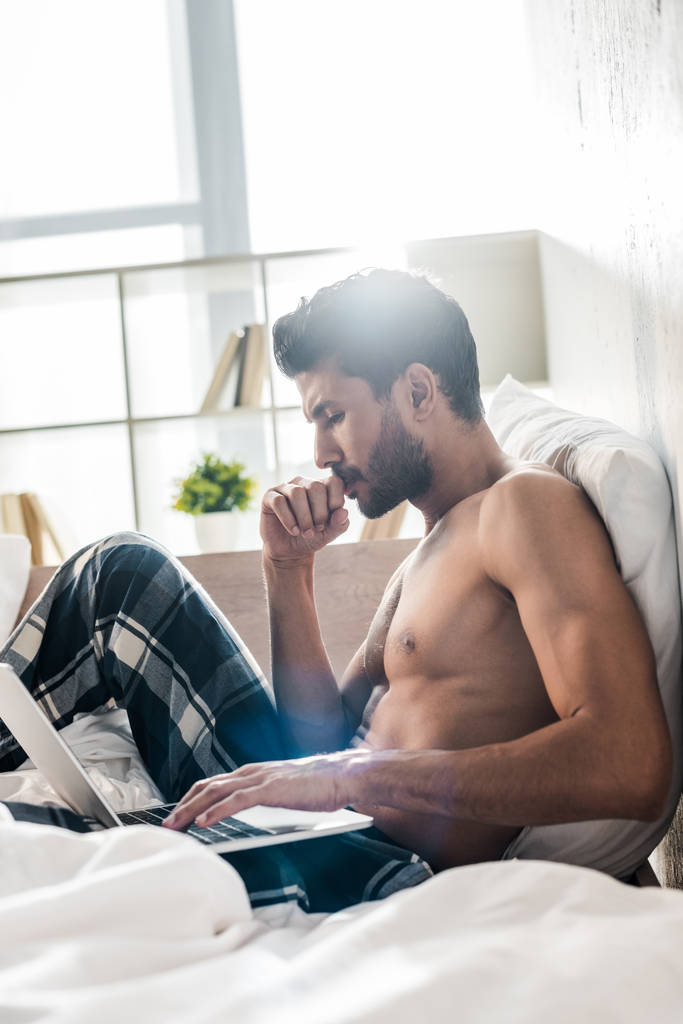 vista lateral del hombre bi-racial guapo y pensativo usando el ordenador portátil en la mañana
  - Foto, imagen