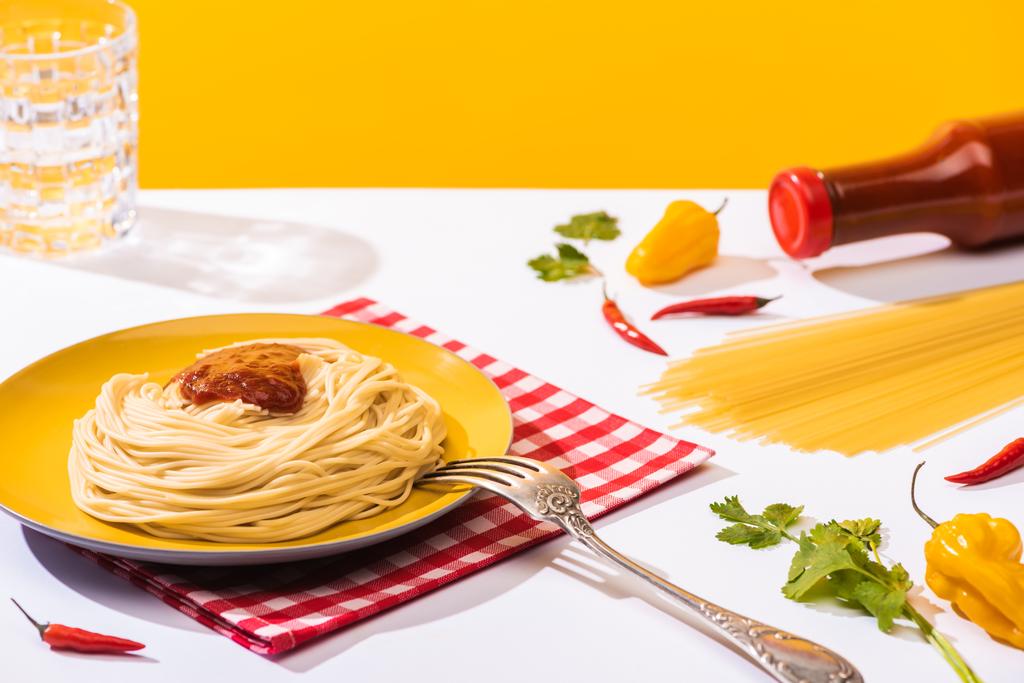 Smaczne spaghetti z ketchupem obok papryki i szklanką wody na białej powierzchni na żółtym tle - Zdjęcie, obraz