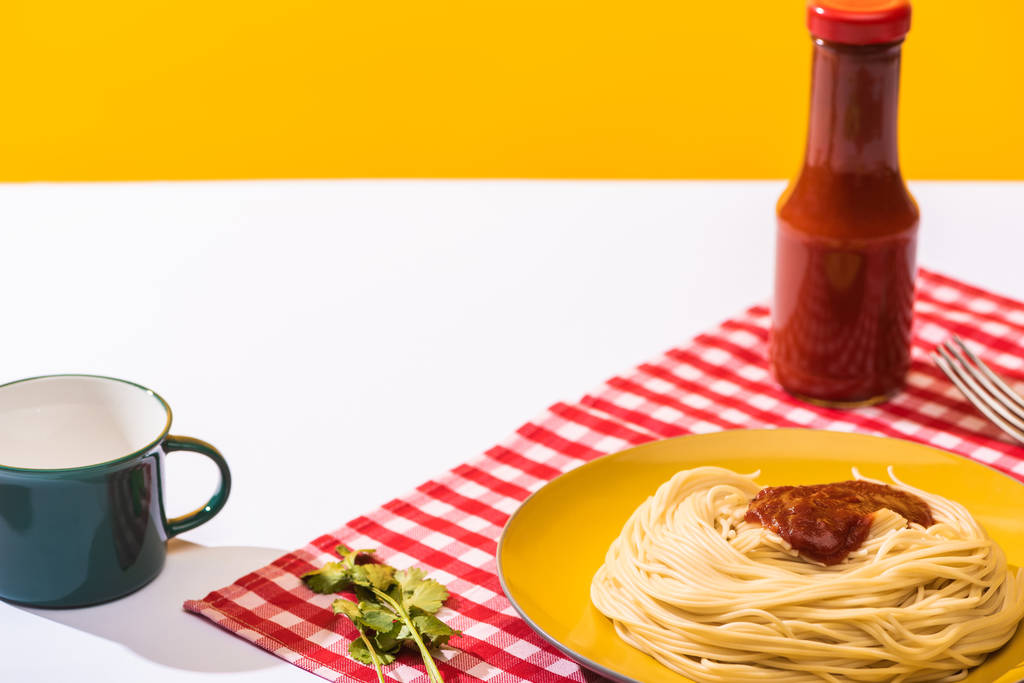 Připravené špagety s rajčatovou omáčkou vedle šálku na bílém povrchu na žlutém pozadí - Fotografie, Obrázek
