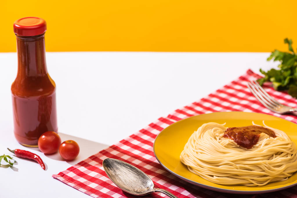 Tomatensaus naast smakelijke spaghetti op witte ondergrond op gele achtergrond - Foto, afbeelding