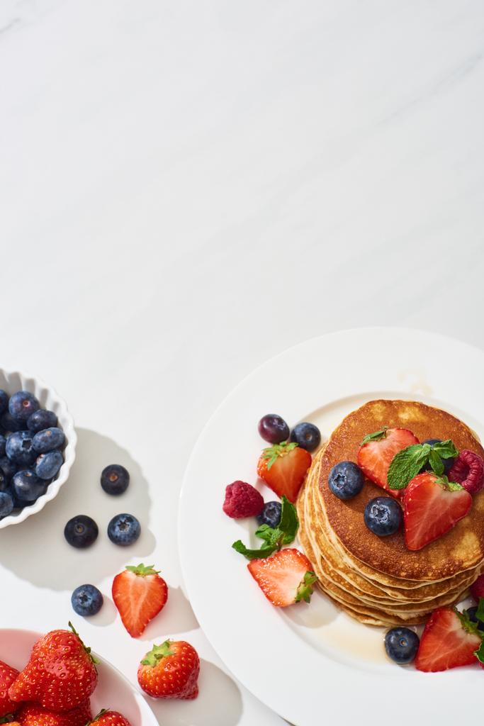 vista superior de deliciosos panqueques con miel, arándanos y fresas en el plato en la superficie blanca de mármol
 - Foto, imagen