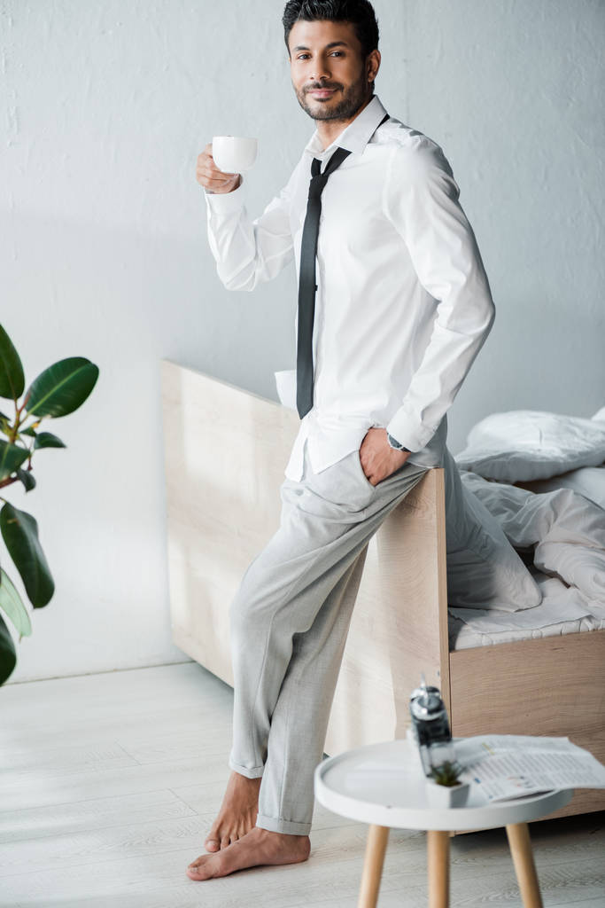 Красивый и улыбающийся бирасовый бизнесмен с чашкой кофе по утрам
  - Фото, изображение
