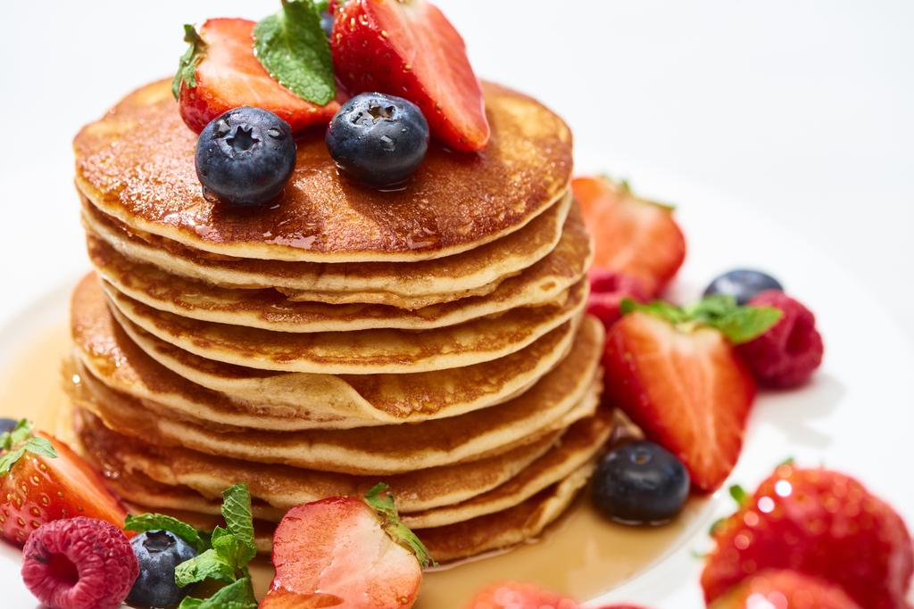 close up view of delicious pancakes with honey, blueberries and strawberries on plate on white surface - Photo, Image