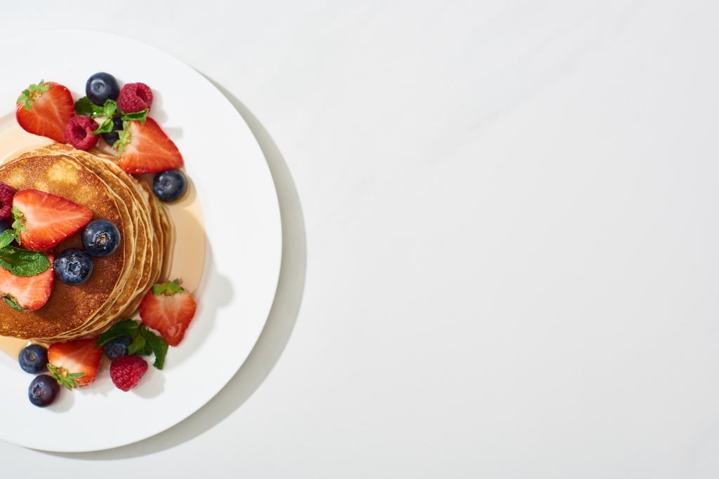 白い大理石の表面にメープルシロップとブルーベリーとイチゴとおいしいパンケーキのトップビュー - 写真・画像