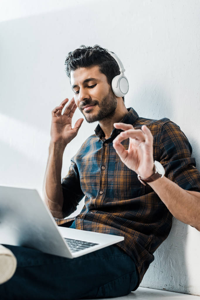 lage hoek uitzicht van knappe en lachende bi-raciale man met laptop luisteren muziek  - Foto, afbeelding