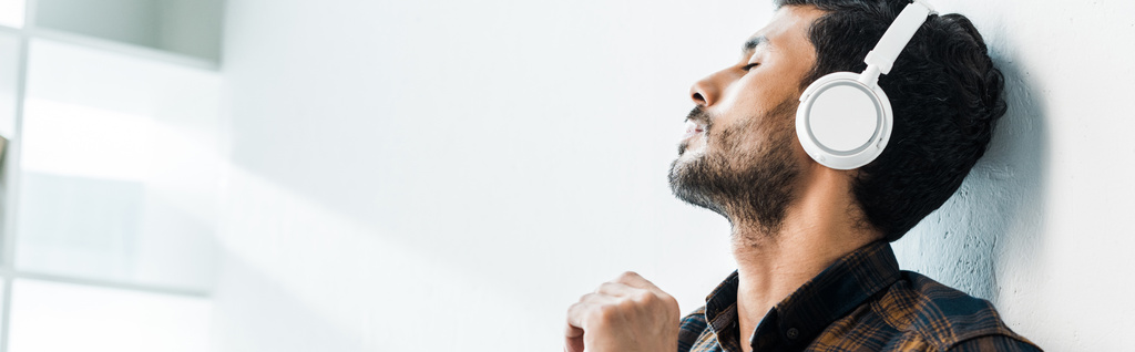 panoráma lövés jóképű bi-rasszista férfi csukott szemmel zenét hallgat  - Fotó, kép