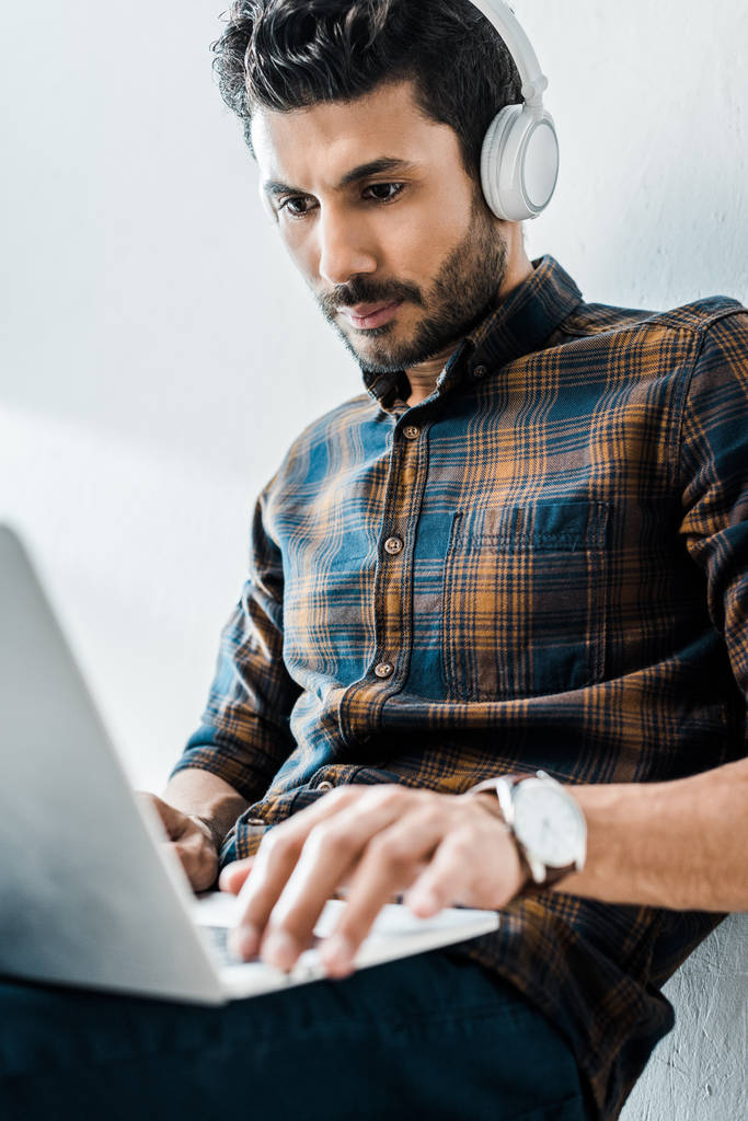 szelektív fókusz jóképű bi-rasszista férfi használó laptop és zenét hallgatni  - Fotó, kép