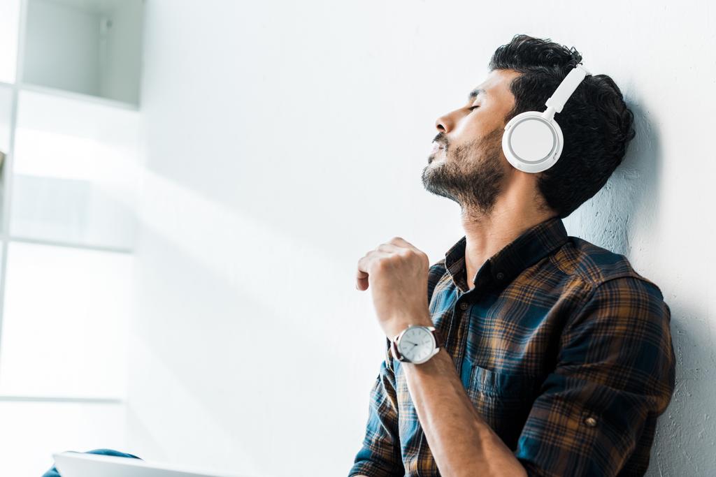 handsome bi-racial man with closed eyes listening music in apartment  - Photo, Image