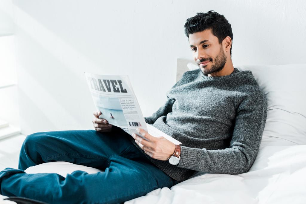 guapo y sonriente bi-racial hombre leyendo periódico con letras de viaje
  - Foto, Imagen