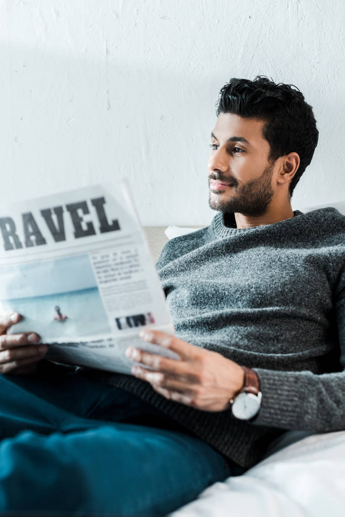 Красивый и улыбающийся двурасовый мужчина держит газету с надписью путешествия
  - Фото, изображение