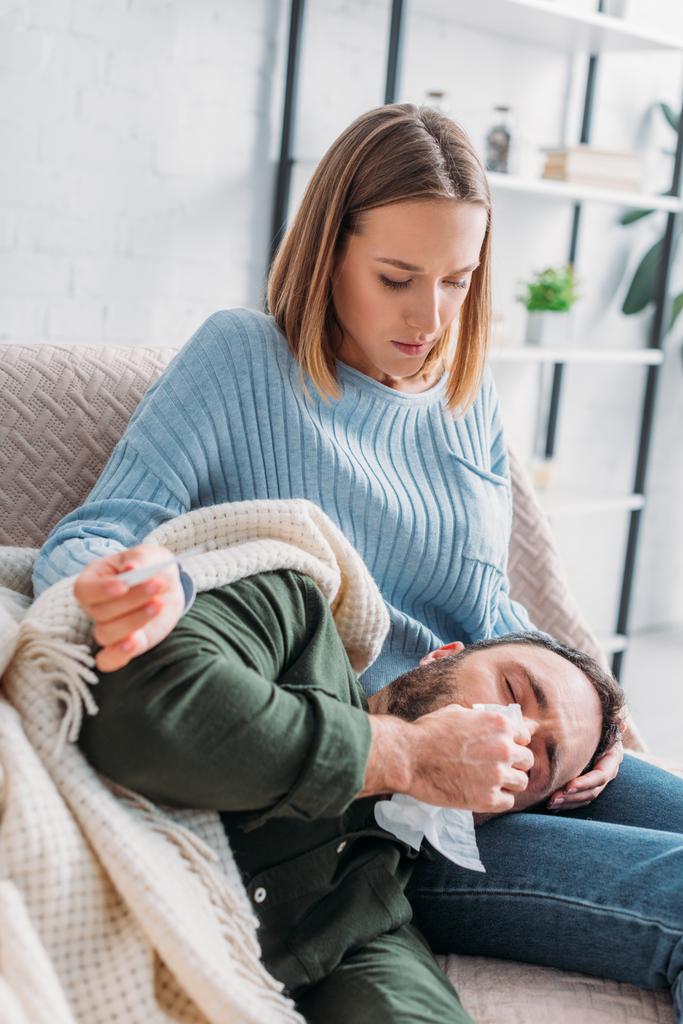 atenta esposa sosteniendo termómetro cerca enfermo marido estornudando mientras acostado en su regazo
 - Foto, imagen