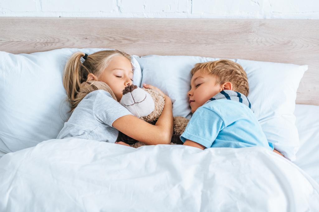 Bruder und Schwester schlafen mit Teddybär im Bett - Foto, Bild