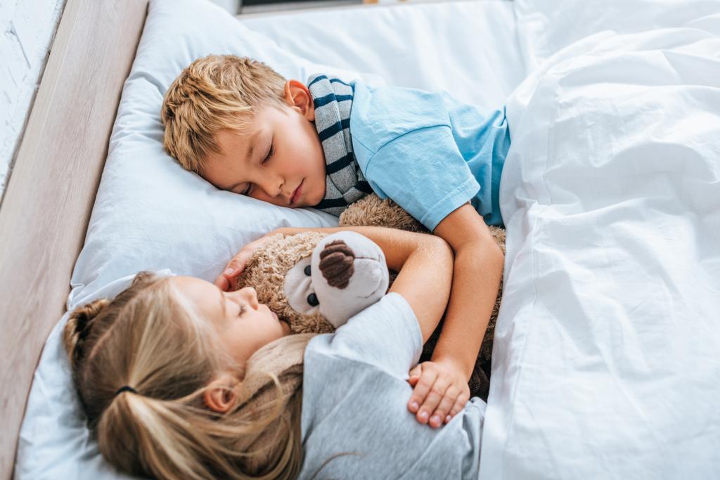 άρρωστοι αδελφός και αδελφή κοιμάται στο κρεβάτι με αρκουδάκι - Φωτογραφία, εικόνα