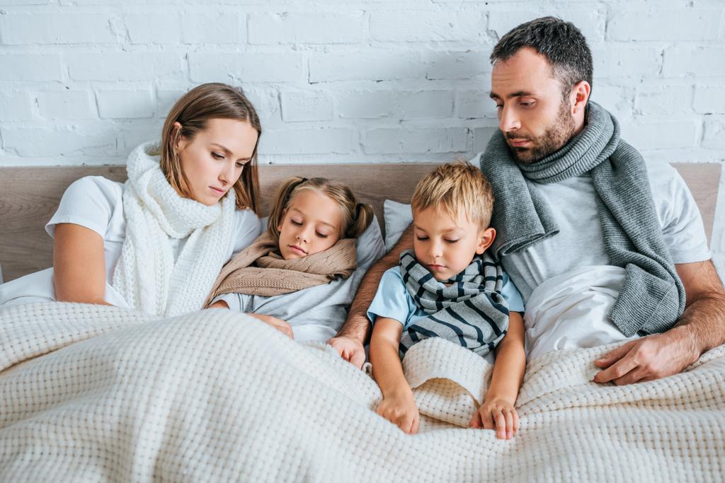 Kranke Familie in warmen Schals unter Decken im Bett liegend - Foto, Bild
