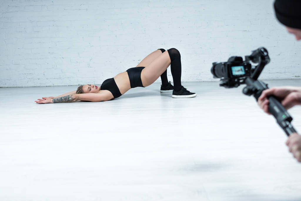 foco seletivo de câmera de tiro menina loira sexy em roupa preta twerking no chão perto da parede de tijolo branco
 - Foto, Imagem