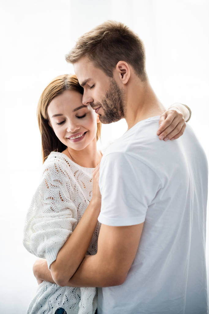 pohledný muž objímání atraktivní a usmívající se žena v bytě  - Fotografie, Obrázek