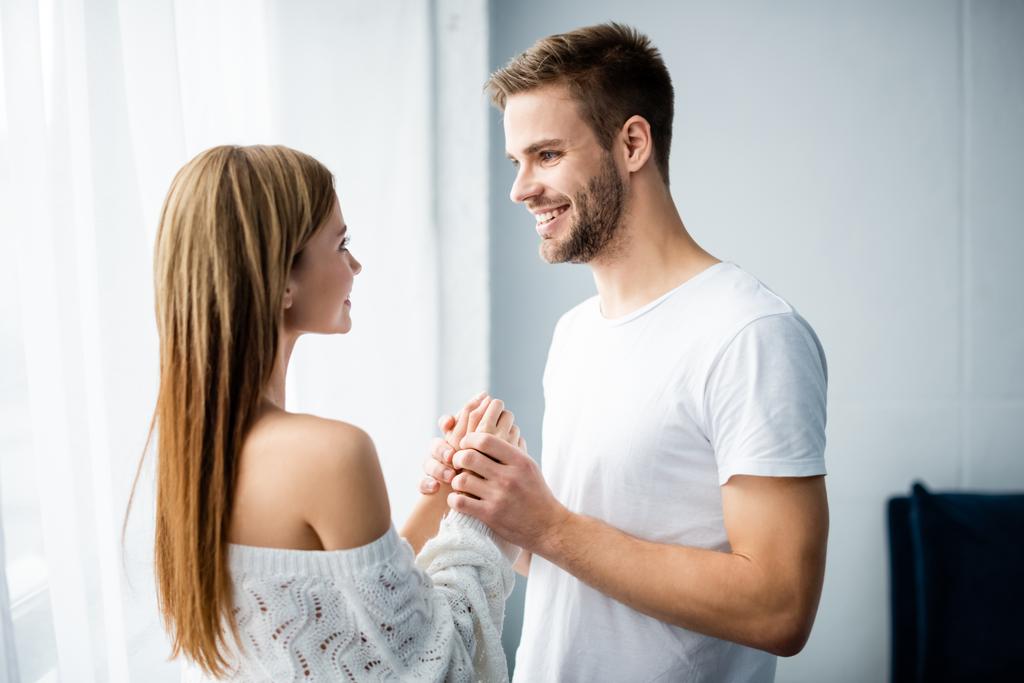 hombre guapo cogido de la mano con la mujer sonriente en el apartamento
  - Foto, Imagen