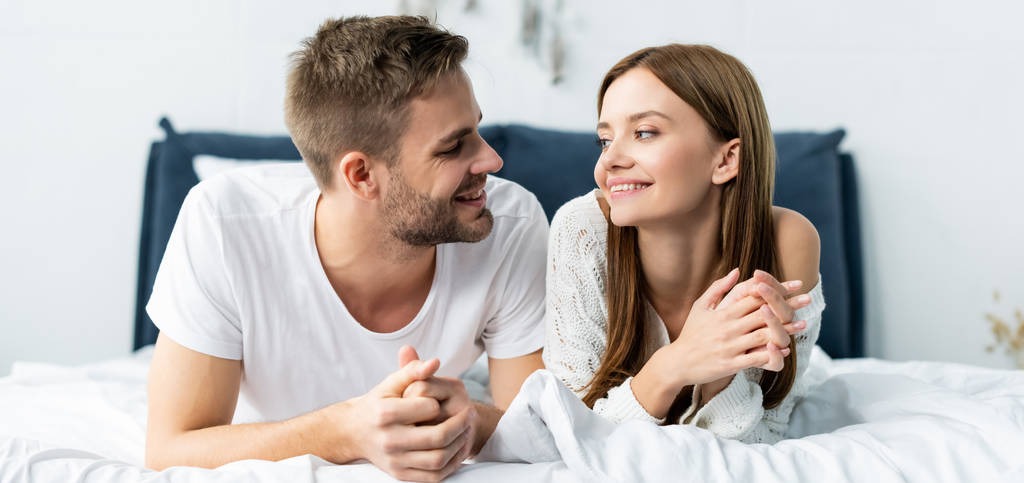 panoramic shot of attractive and smiling woman looking at handsome man in apartment  - Photo, Image