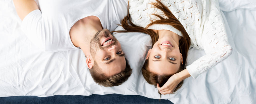 панорамный снимок красивого мужчины и улыбающейся женщины, смотрящей на камеру в квартире
 - Фото, изображение