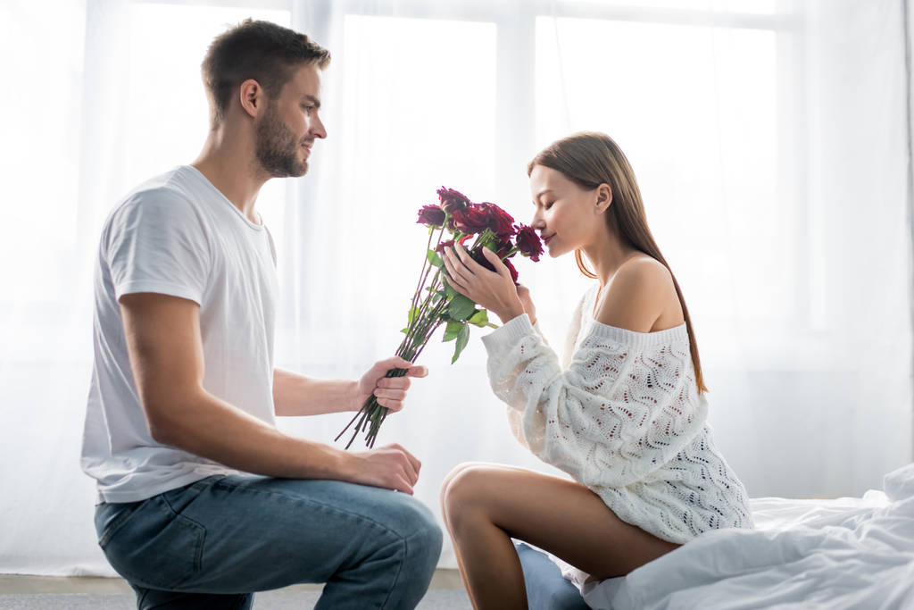 side view of handsome man giving bouquet to attractive woman in apartment  - Photo, Image