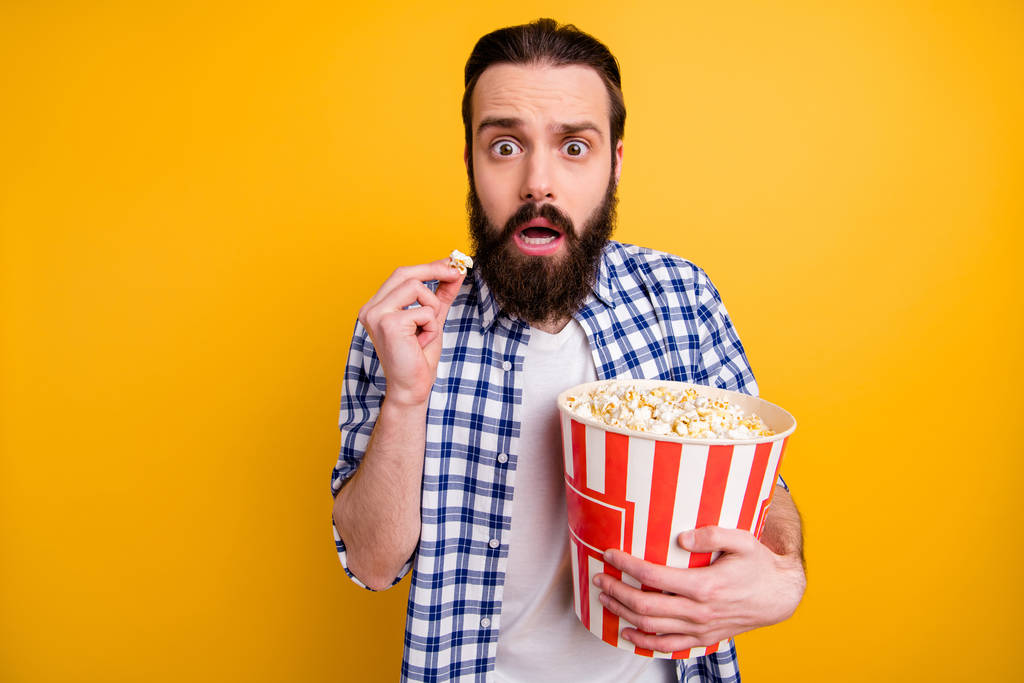 Portrait of nice attractive worried scared addicted bearded guy in checked shirt overeating popcorn junk snack watching scary video isolated over bright vivid shine vibrant yellow color background - Photo, Image