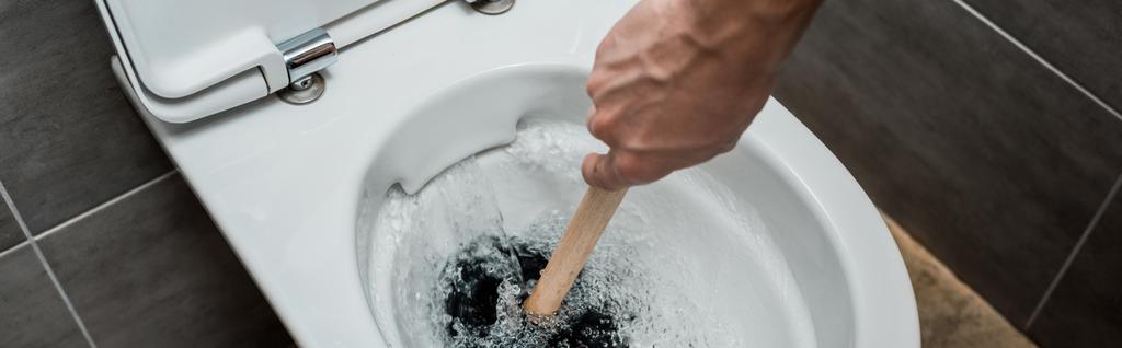 обрезанный вид водопроводчика с помощью вантуза в унитазе во время смыва в современном туалете с серой плиткой, панорамный снимок
 - Фото, изображение
