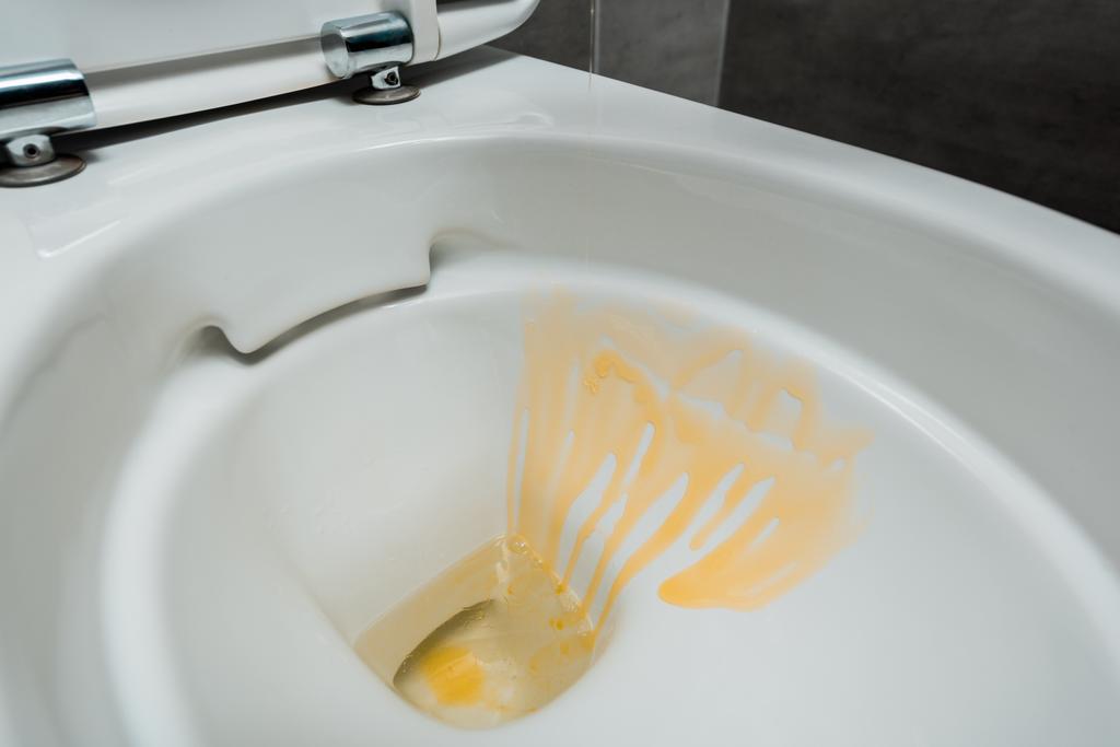 στενή άποψη του κίτρινου υγρού απορρυπαντικού σε κεραμική καθαρή λεκάνη τουαλέτας στη σύγχρονη τουαλέτα με γκρι πλακάκι - Φωτογραφία, εικόνα
