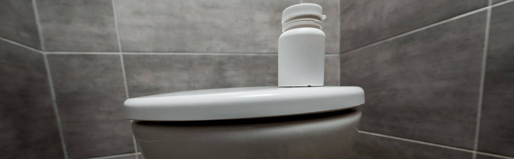 pojemnik z tabletkami na ceramiczne czyste muszle klozetowe w nowoczesnej toalecie z szarą płytką, panoramiczne ujęcie - Zdjęcie, obraz